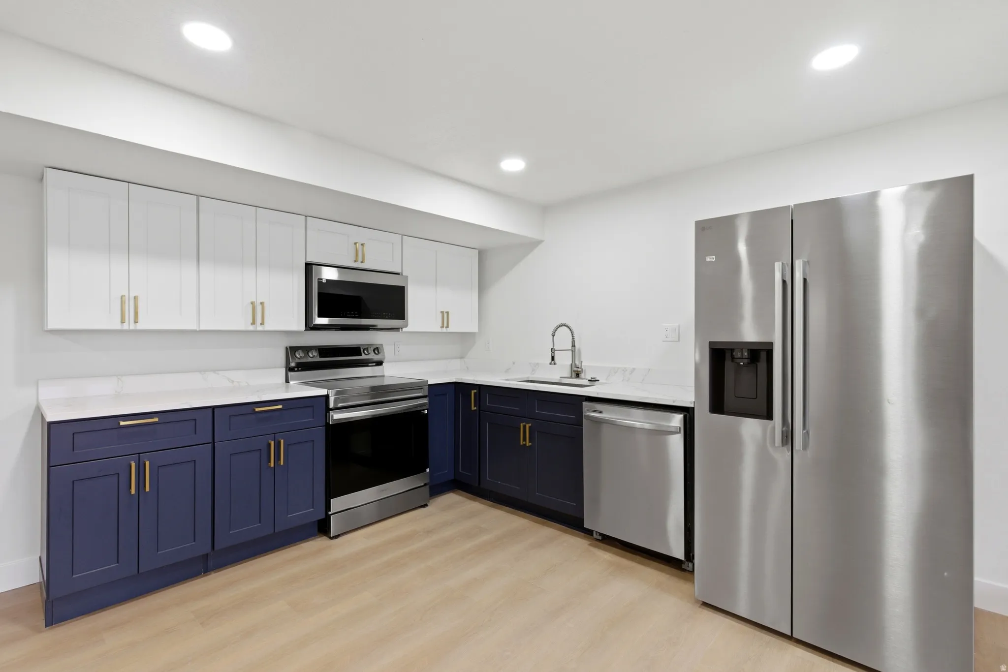 Two tone kitchen with stainless steel appliances, two tone color scheme, light wood-style floors, light stone counters, and recessed lighting