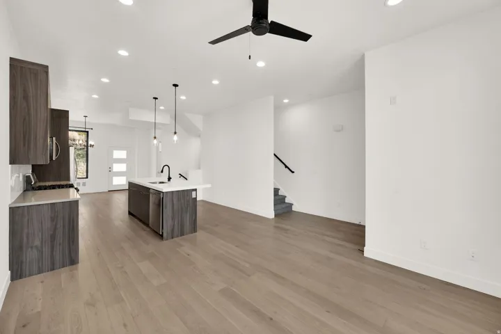 Kitchen with dark wood finish cabinetry, open floor plan, a center island with sink, a ceiling fan, and light wood-style flooring