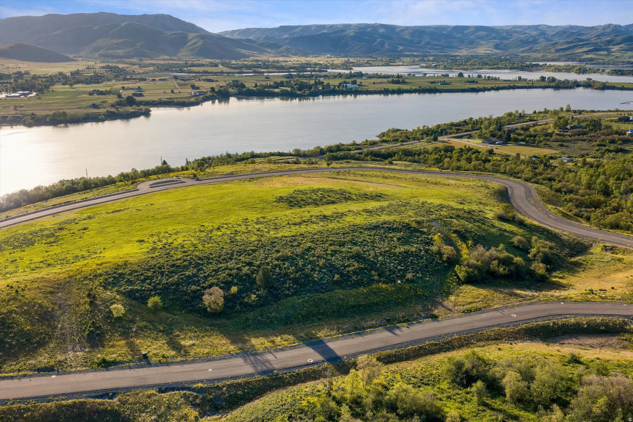 Expansive land parcel featuring paved roads, lush green and shrub vegetation, and surrounding water bodies with distant mountains
