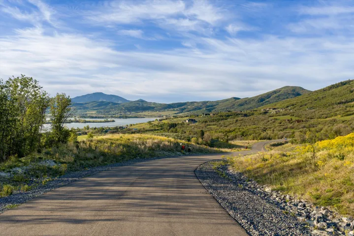 Paved road winding through a natural landscape featuring distant mountains, a body of water, and scattered residences