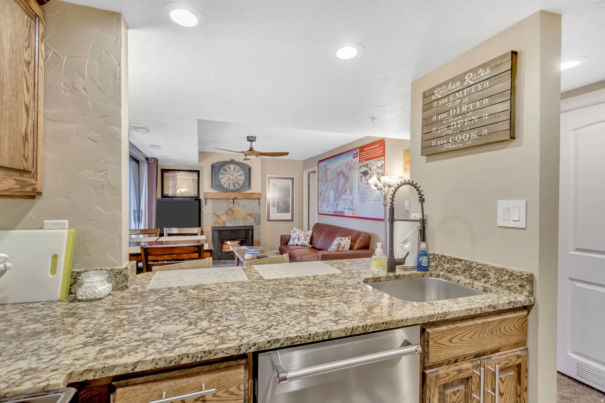 Kitchen featuring stainless steel dishwasher, a fireplace, brown cabinets, ceiling fan, and recessed lighting