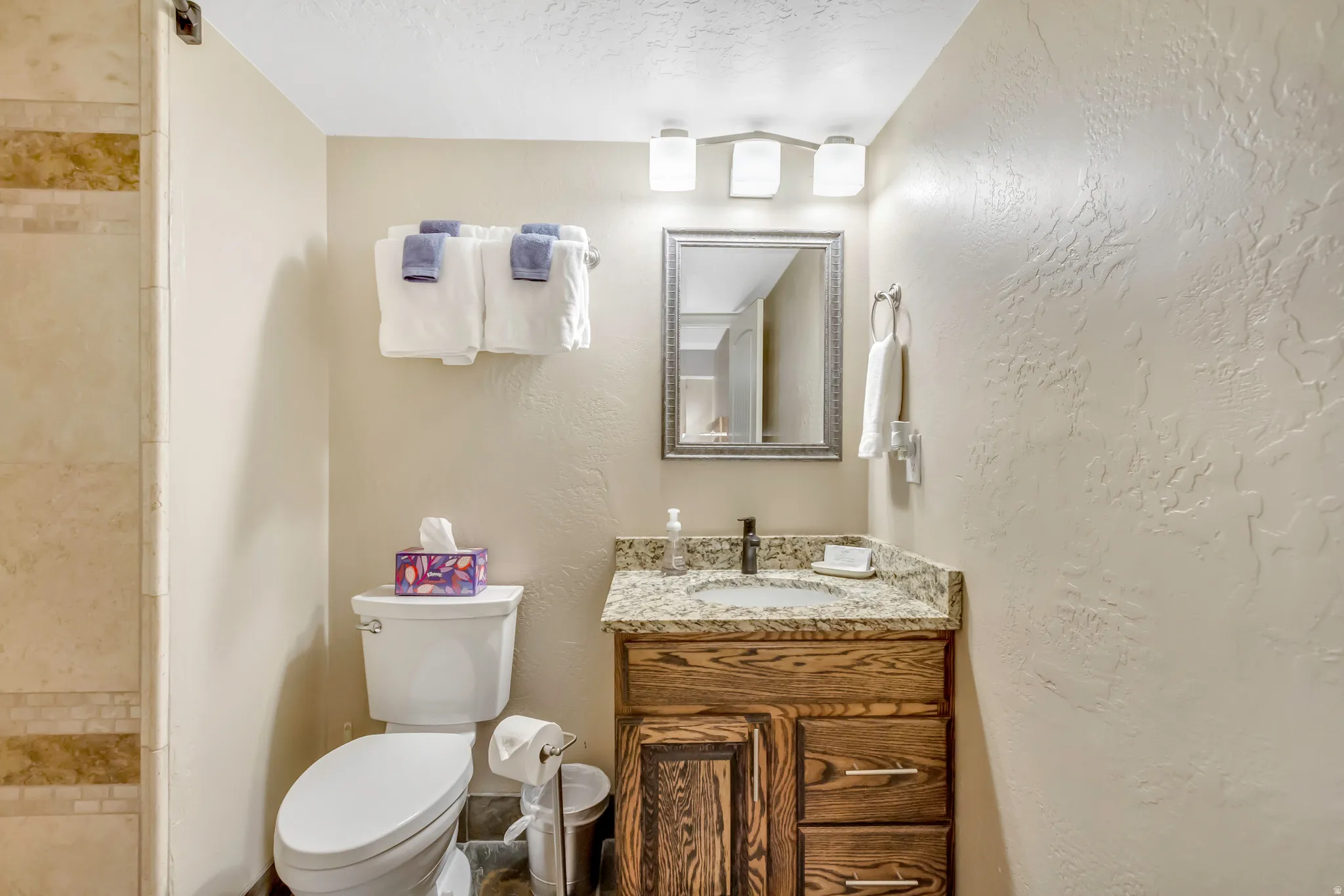 Bathroom with a textured ceiling, vanity, a textured wall, and tiled shower