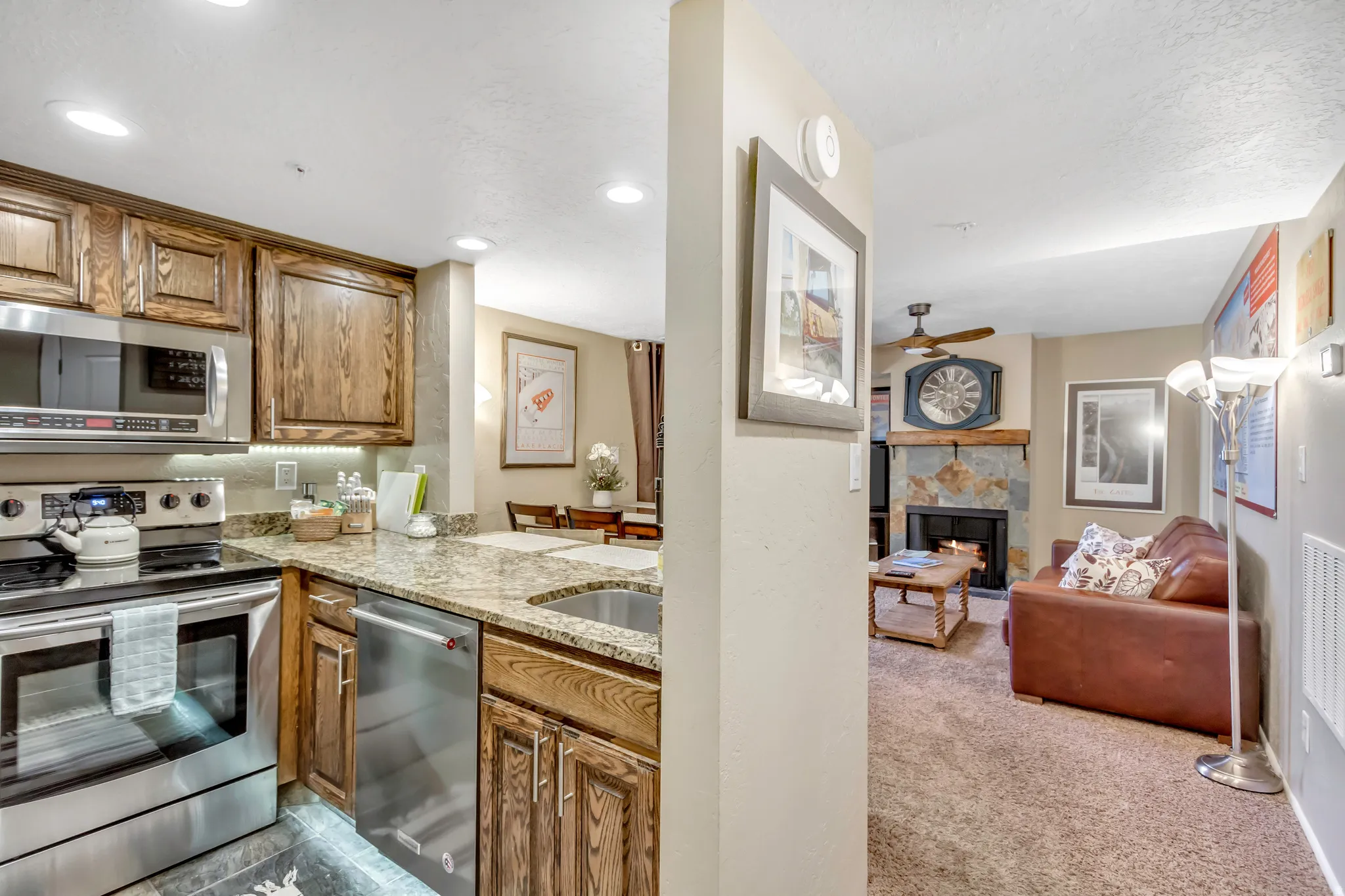 Kitchen featuring appliances with stainless steel finishes, light stone counters, a lit fireplace, light colored carpet, and brown cabinetry