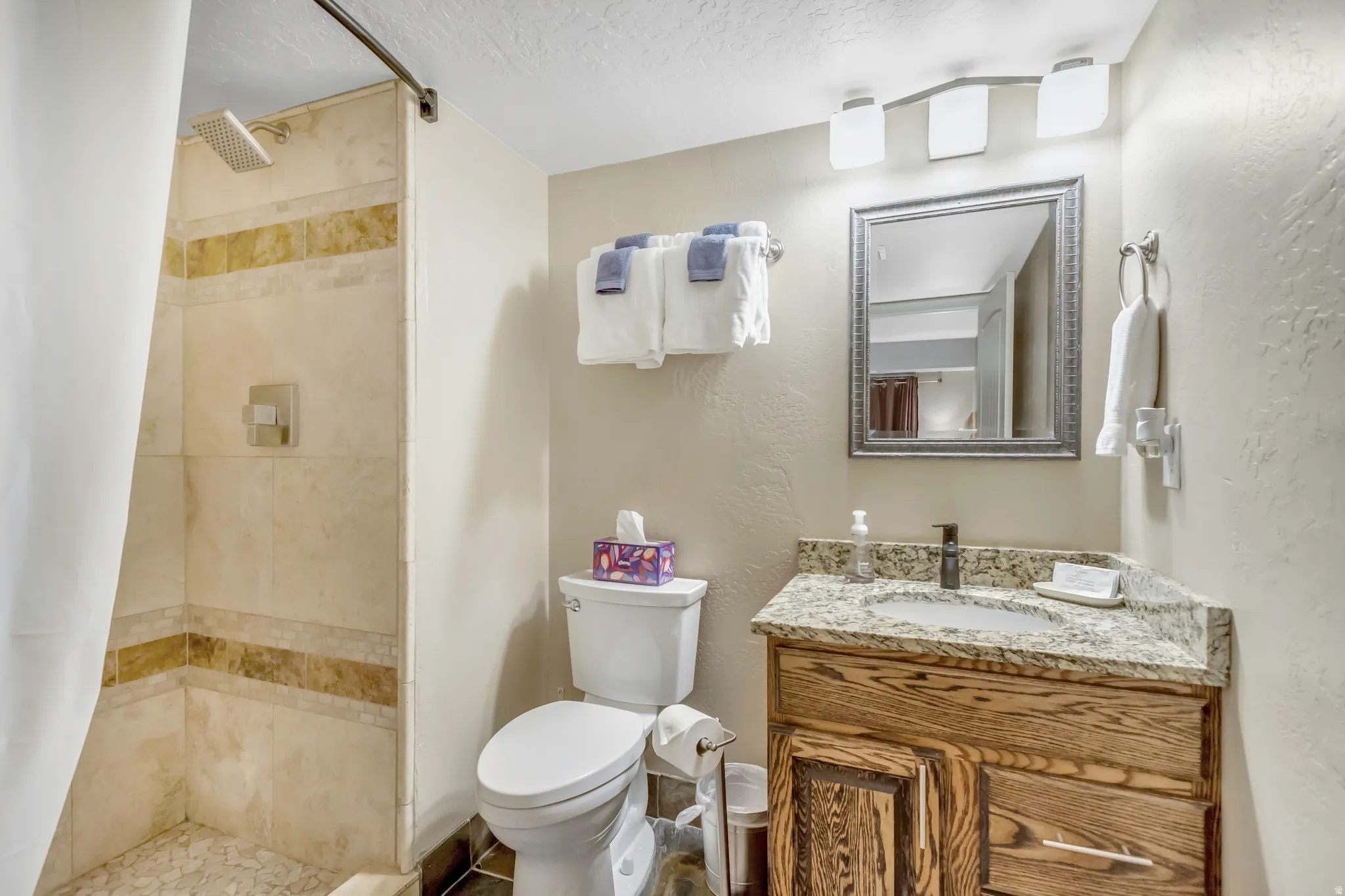Bathroom with a shower stall, vanity, a textured ceiling, and a textured wall