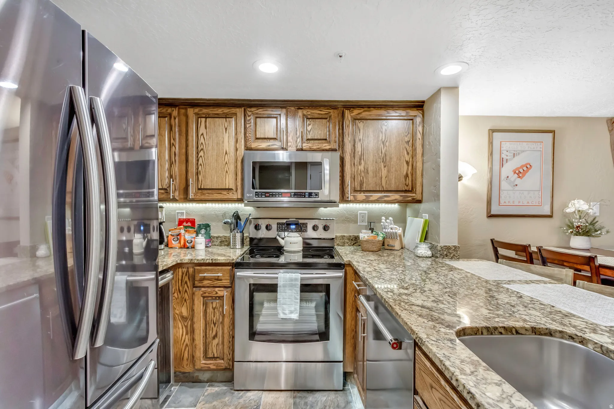 Kitchen with appliances with stainless steel finishes, light stone countertops, brown cabinetry, a textured ceiling, and recessed lighting