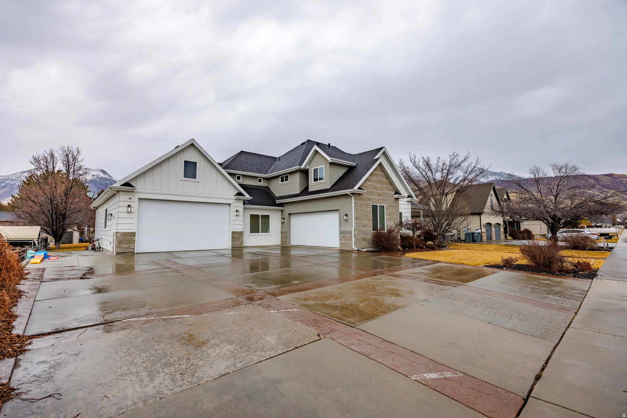 View of front of home featuring board and batten siding, stone siding, driveway, and a shingled roof