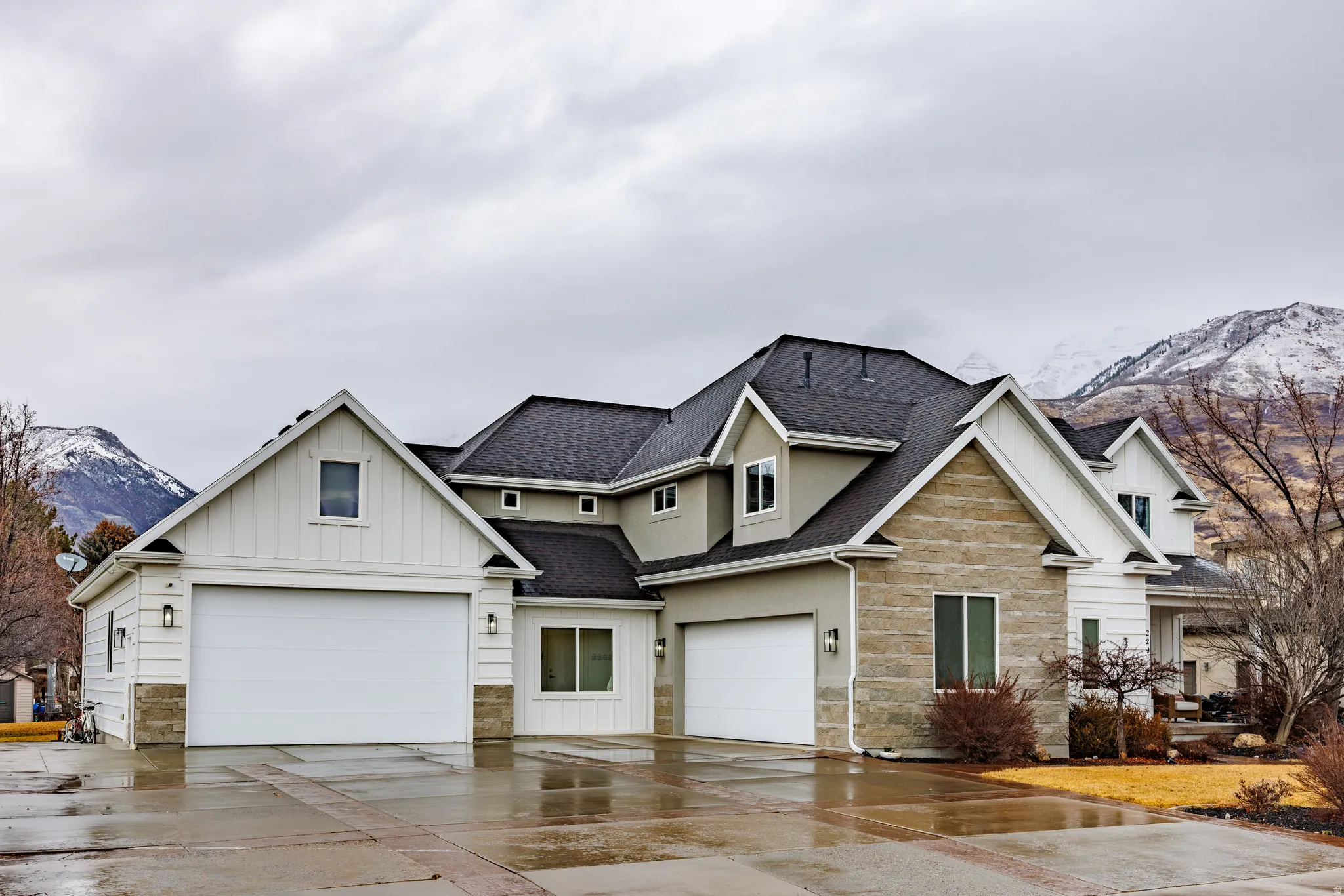 View of front of home with a mountain view, board and batten siding, roof with shingles, stone siding, and driveway