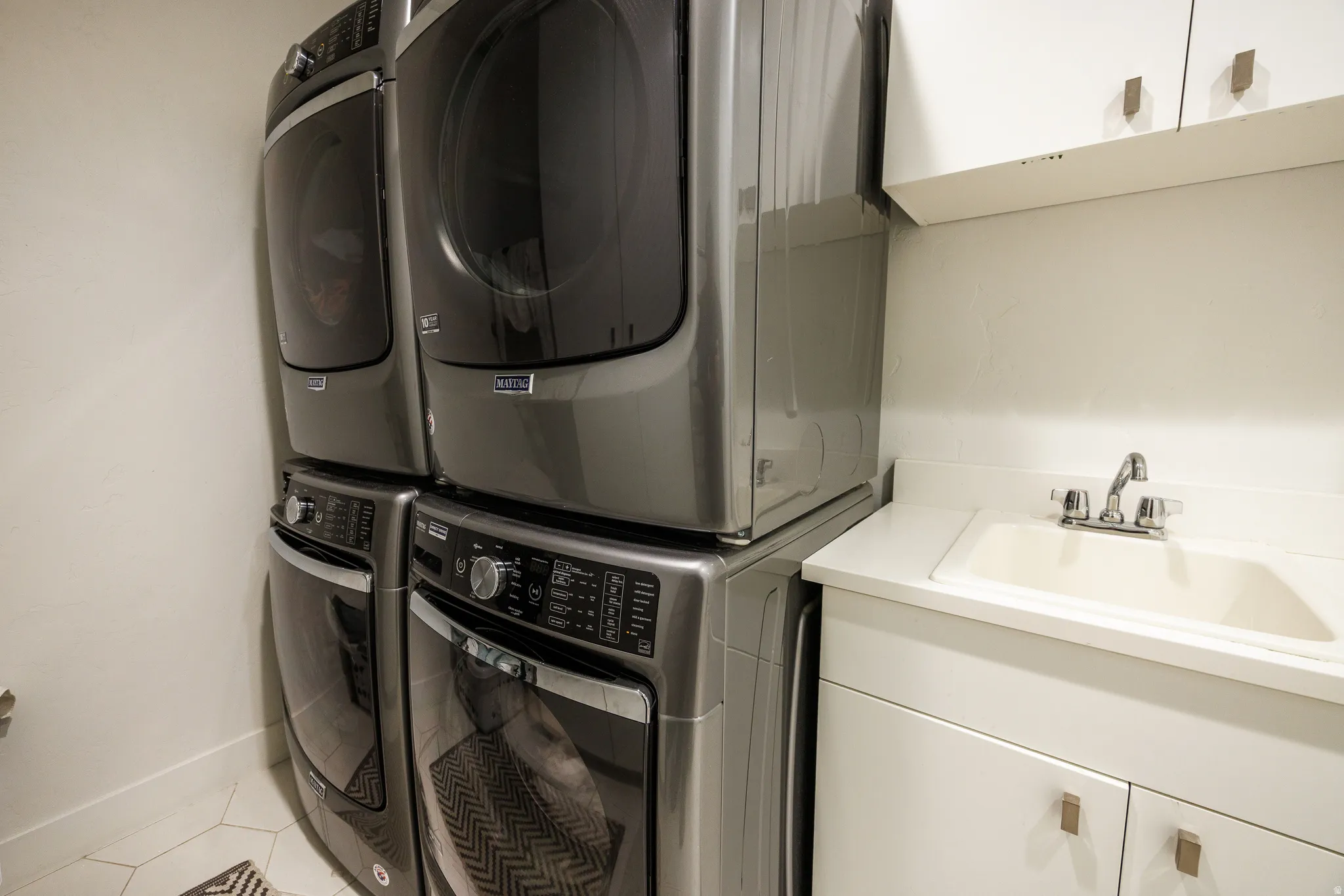 Laundry room with cabinet space, stacked washer / dryer, and tile patterned flooring
