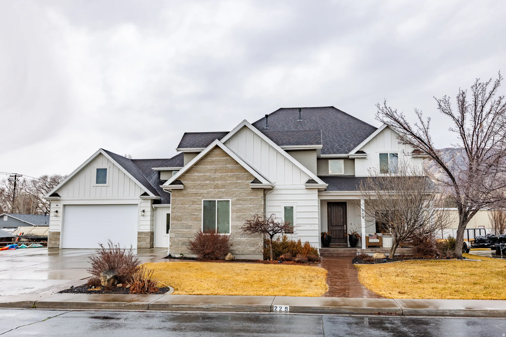 View of front facade with a shingled roof, board and batten siding, concrete driveway, a garage, and stone siding