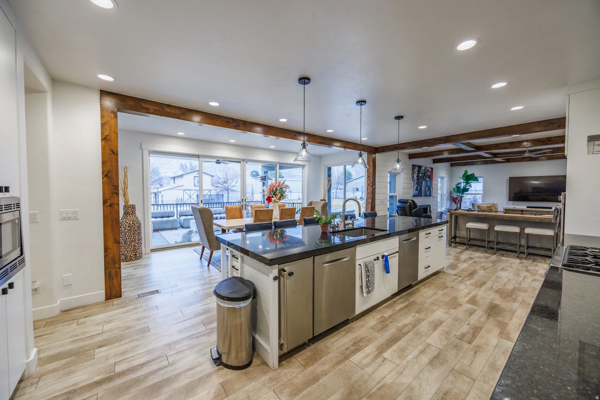 Kitchen with pendant lighting, light wood-type flooring, an island with sink, open floor plan, and beamed ceiling