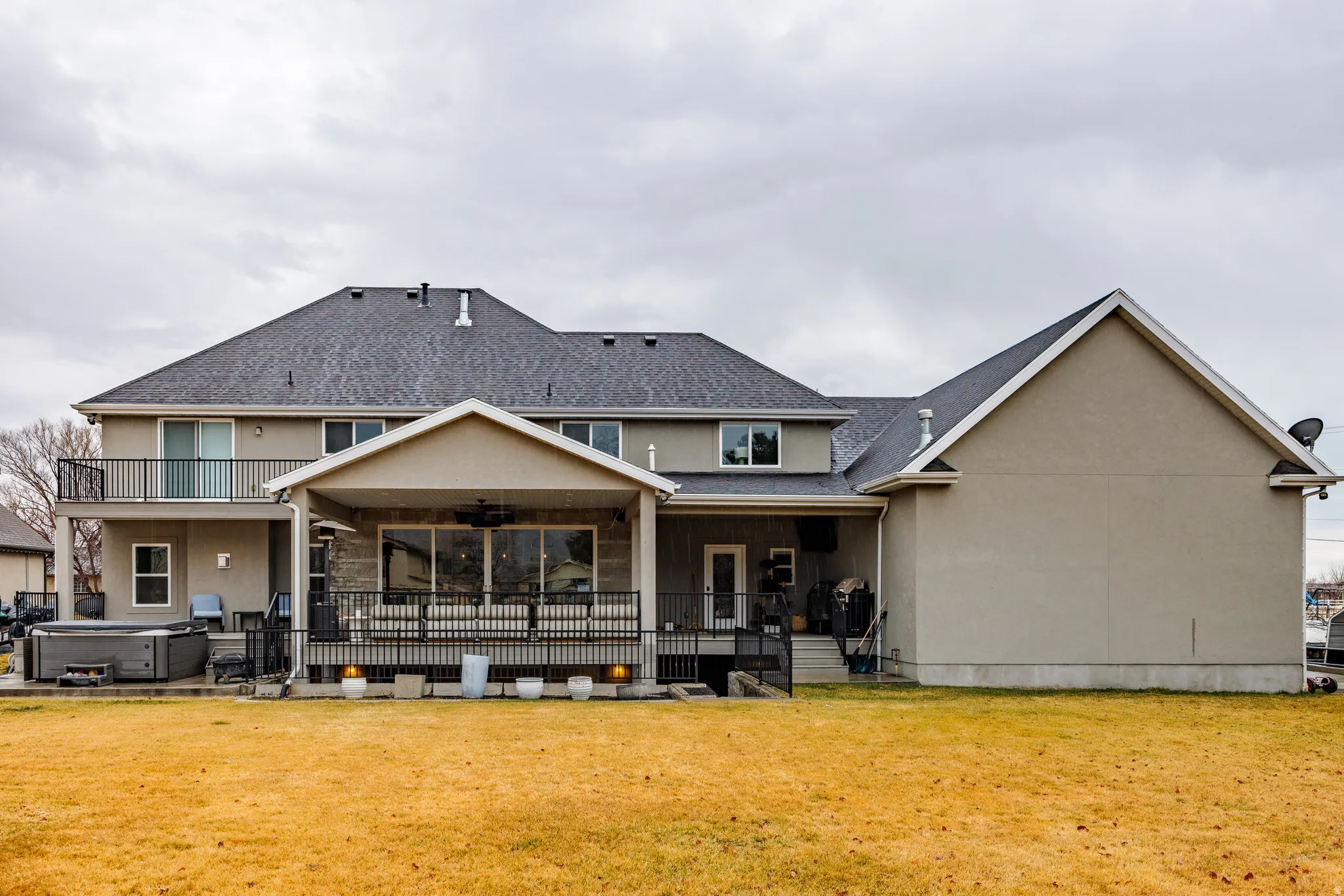 Back of house featuring a ceiling fan, a hot tub, stucco siding, a patio area, and a lawn
