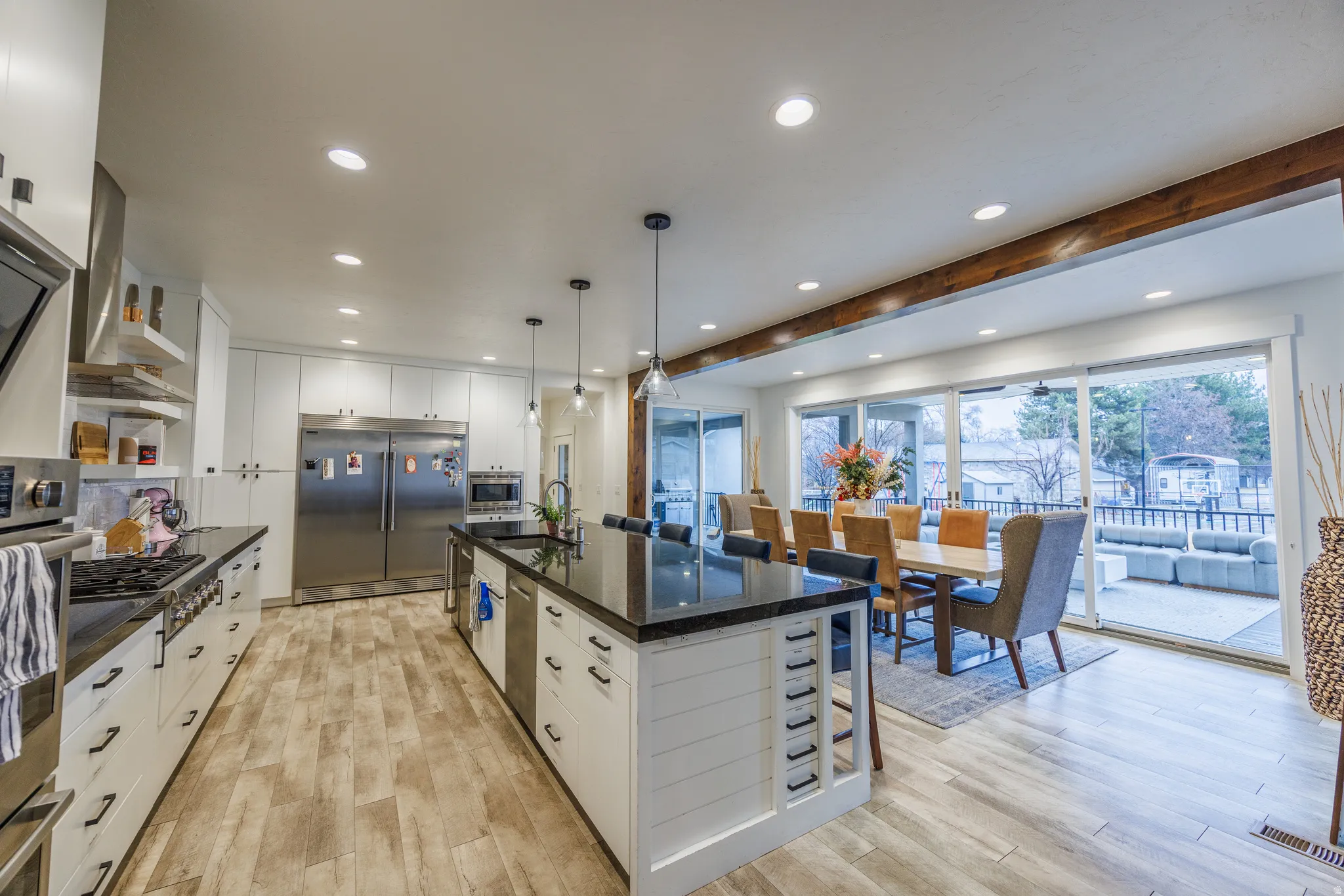 Kitchen with white cabinetry, decorative light fixtures, built in appliances, a large island with sink, and light wood-type flooring