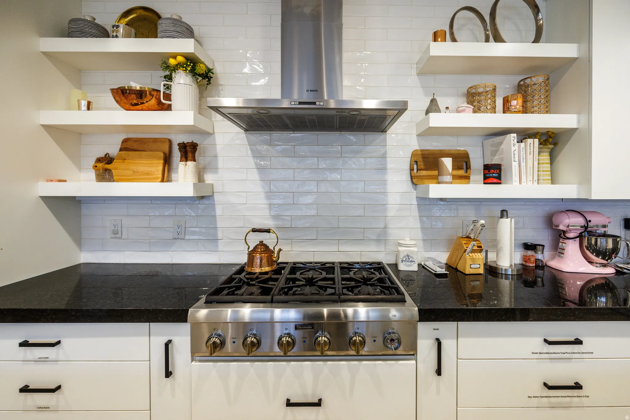 Kitchen with open shelves, stainless steel gas cooktop, dark stone countertops, and white cabinetry