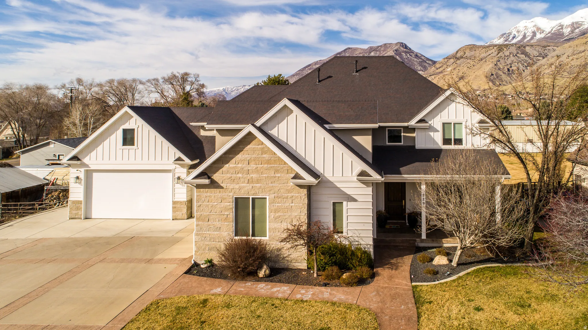 View of front of home with board and batten siding, concrete driveway, stone siding, and a shingled roof