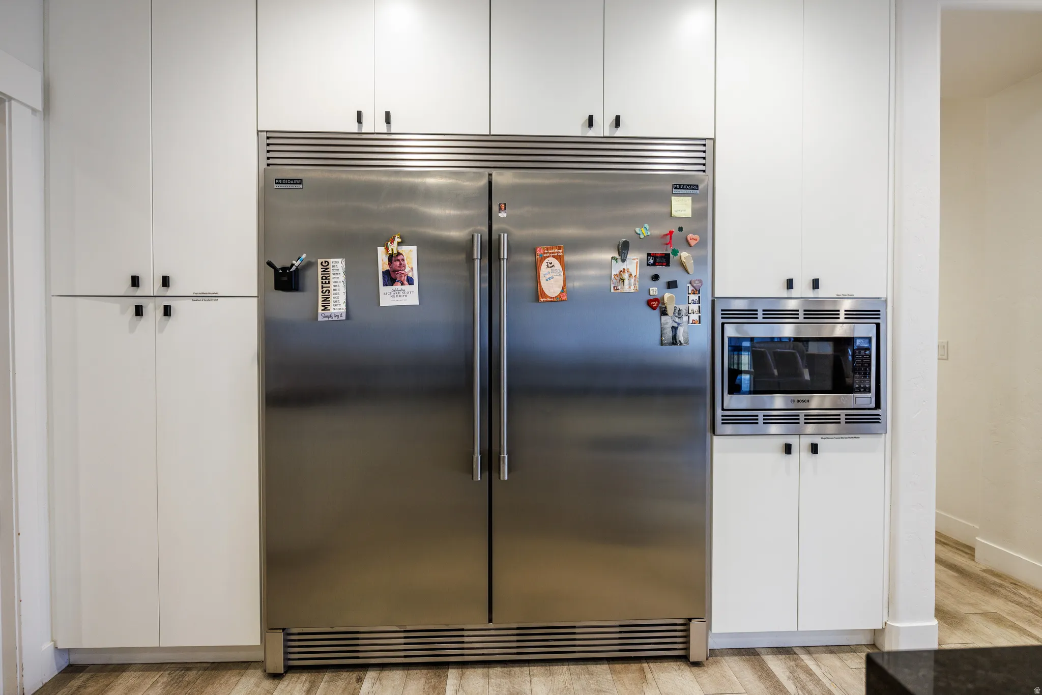 Detailed view of built in appliances, white cabinets, and light wood-type flooring