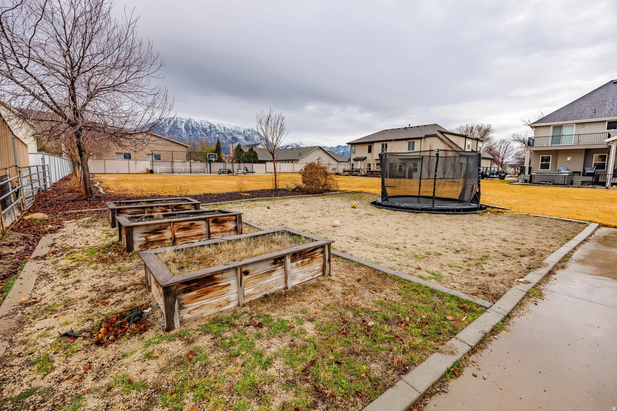 Fenced yard with a trampoline, a residential view, a vegetable garden, and a mountain view
