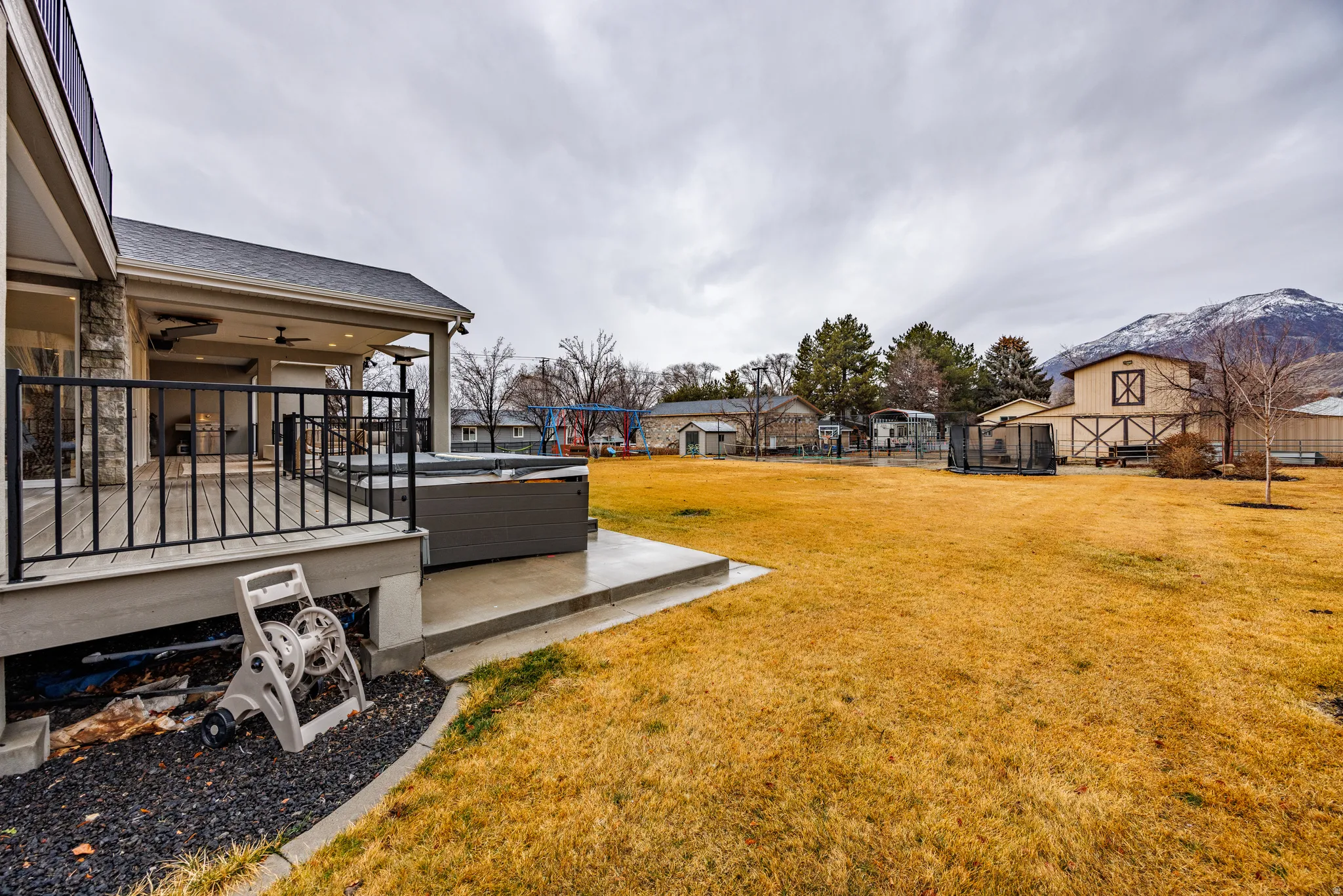 View of yard featuring a trampoline, a hot tub, a ceiling fan, a residential view, and a playground
