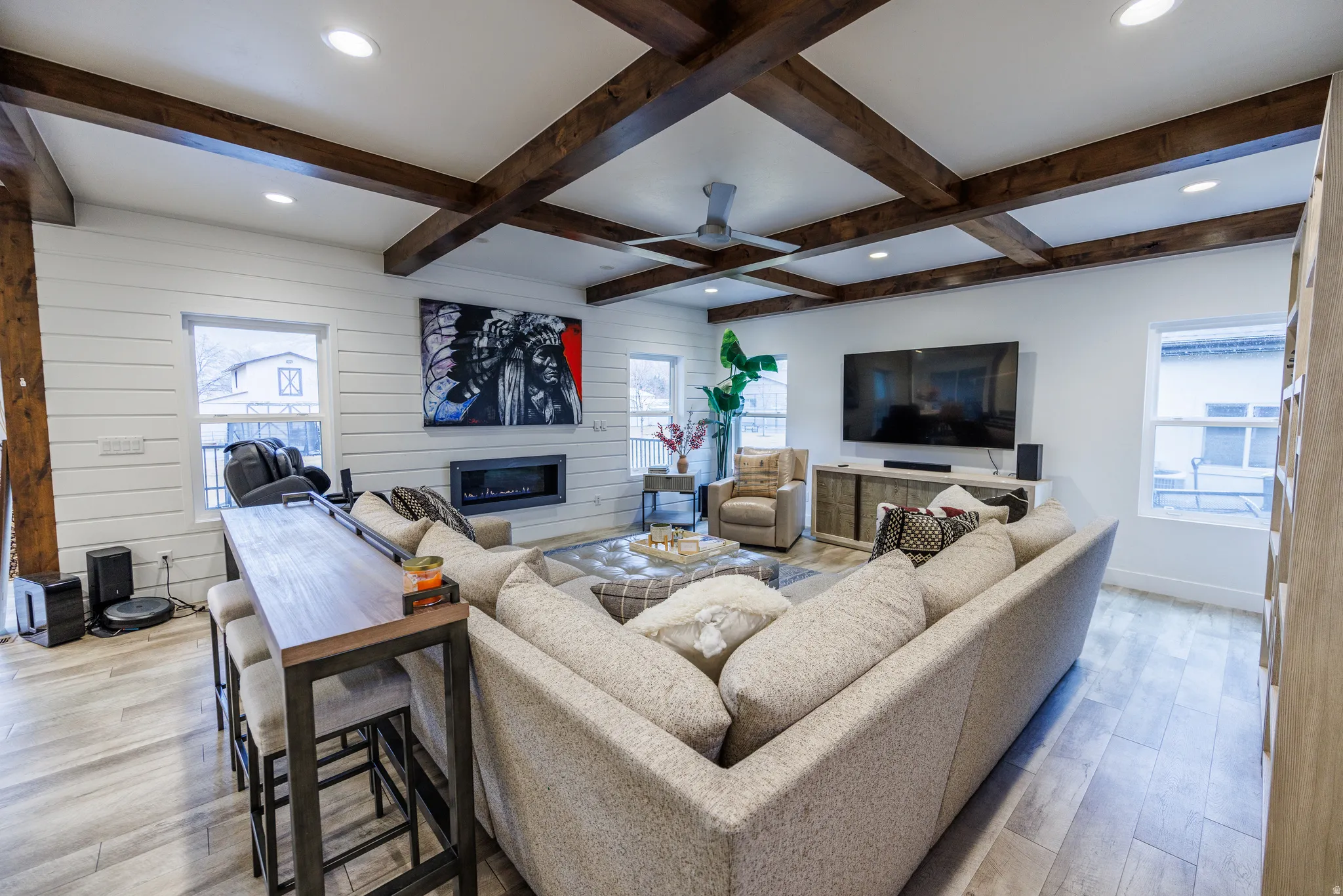 Living area with light wood-type flooring, a ceiling fan, a glass covered fireplace, wooden walls, and recessed lighting