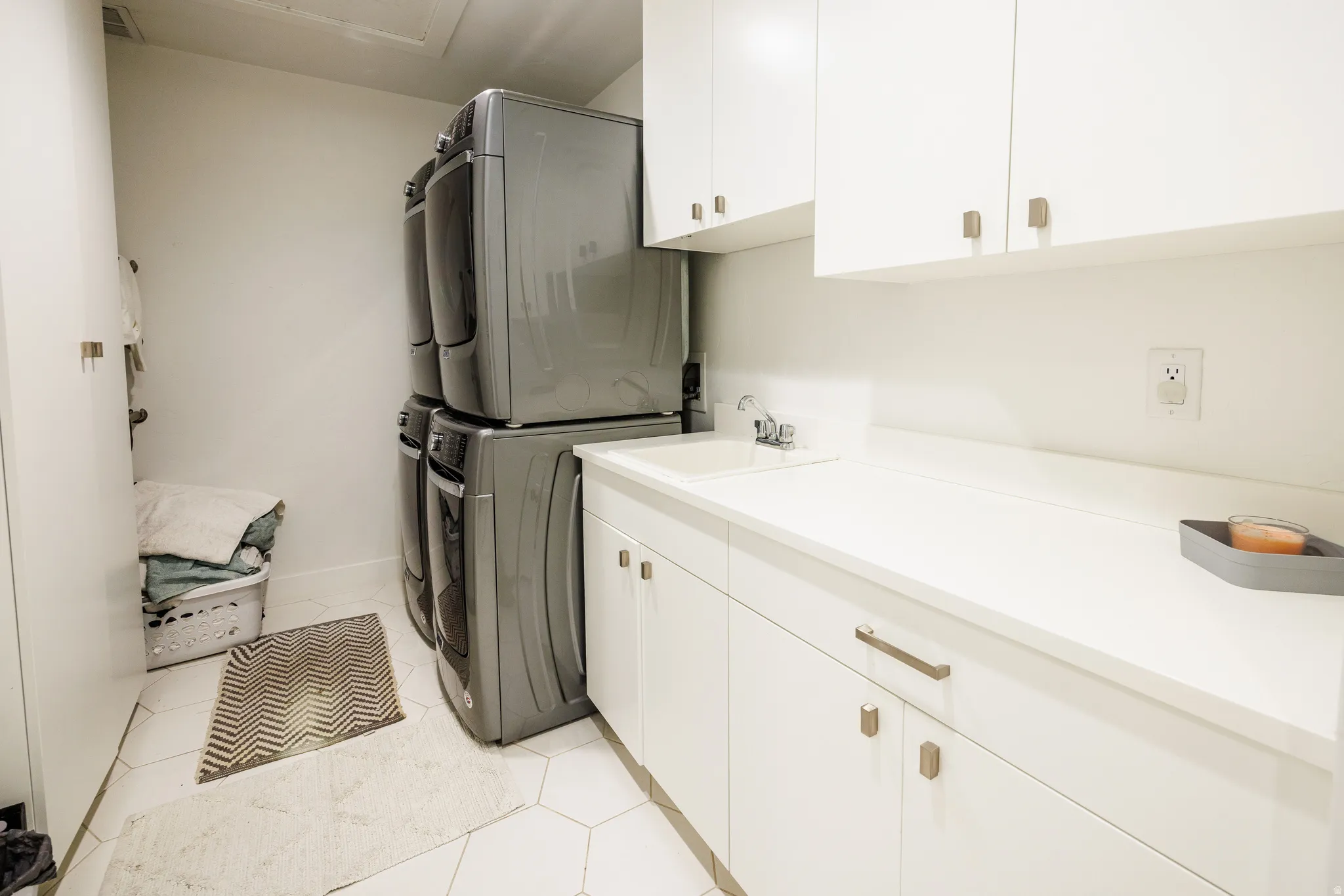 Laundry area featuring cabinet space, stacked washing machine and dryer, and light tile patterned floors