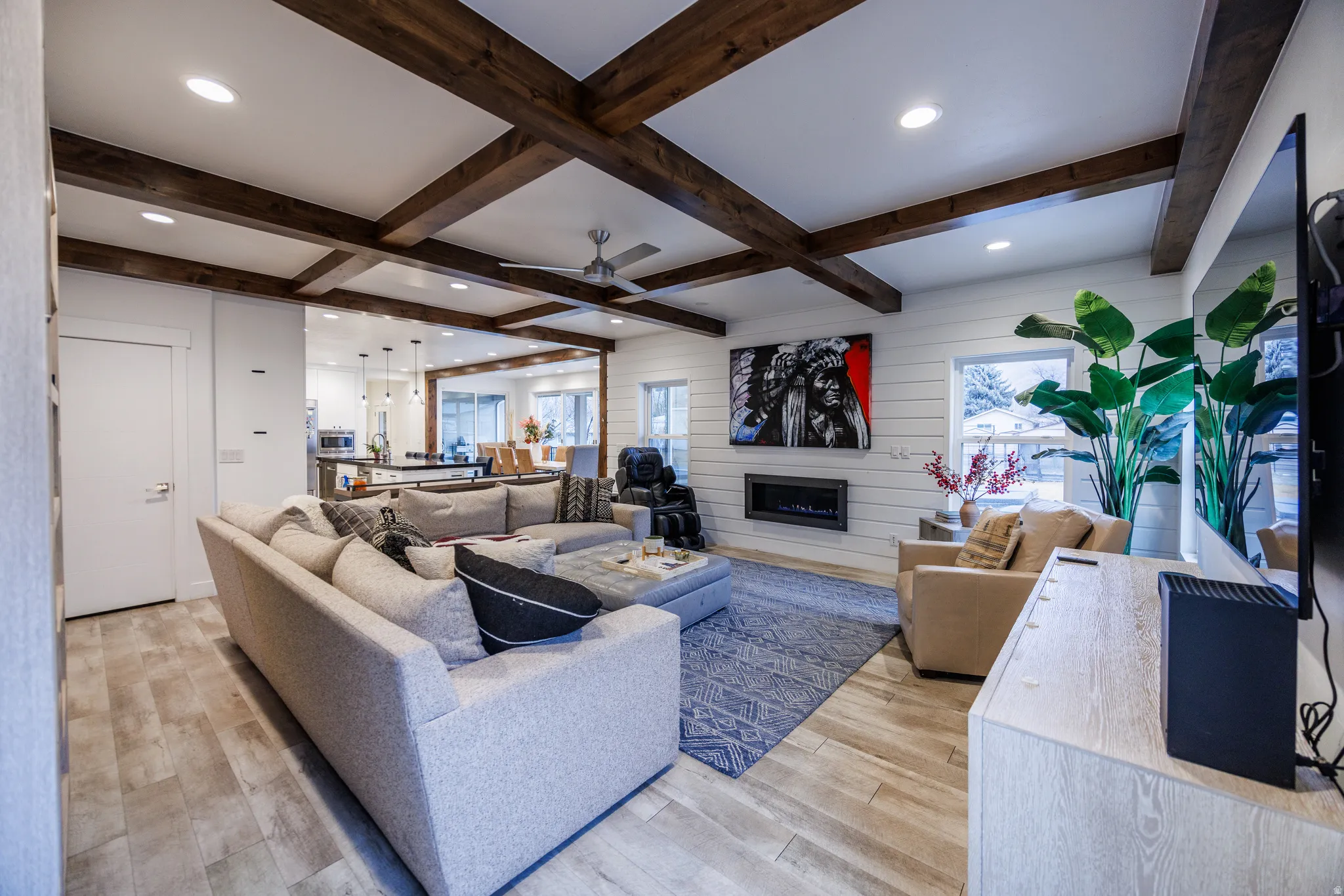 Living area with light wood-type flooring, a glass covered fireplace, ceiling fan, recessed lighting, and wood walls