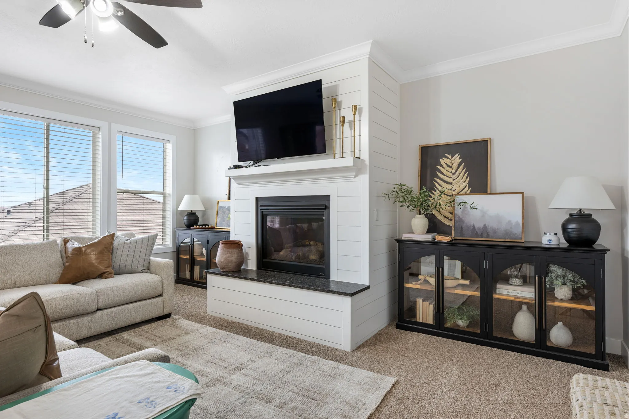 Living area with carpet, crown molding, a glass covered fireplace, and ceiling fan