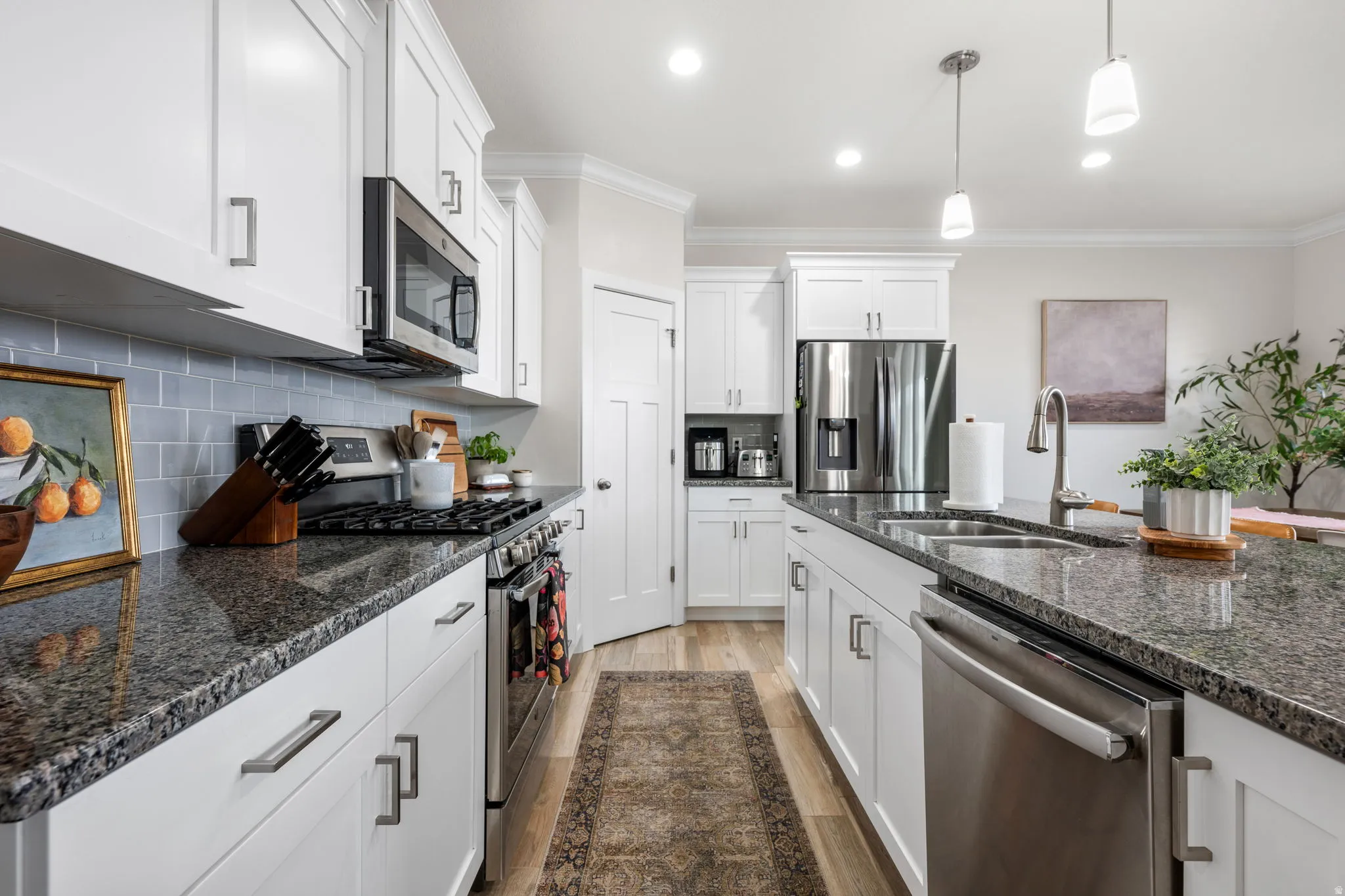 Kitchen with stainless steel appliances, dark stone countertops, ornamental molding, white cabinets, and light wood finished floors