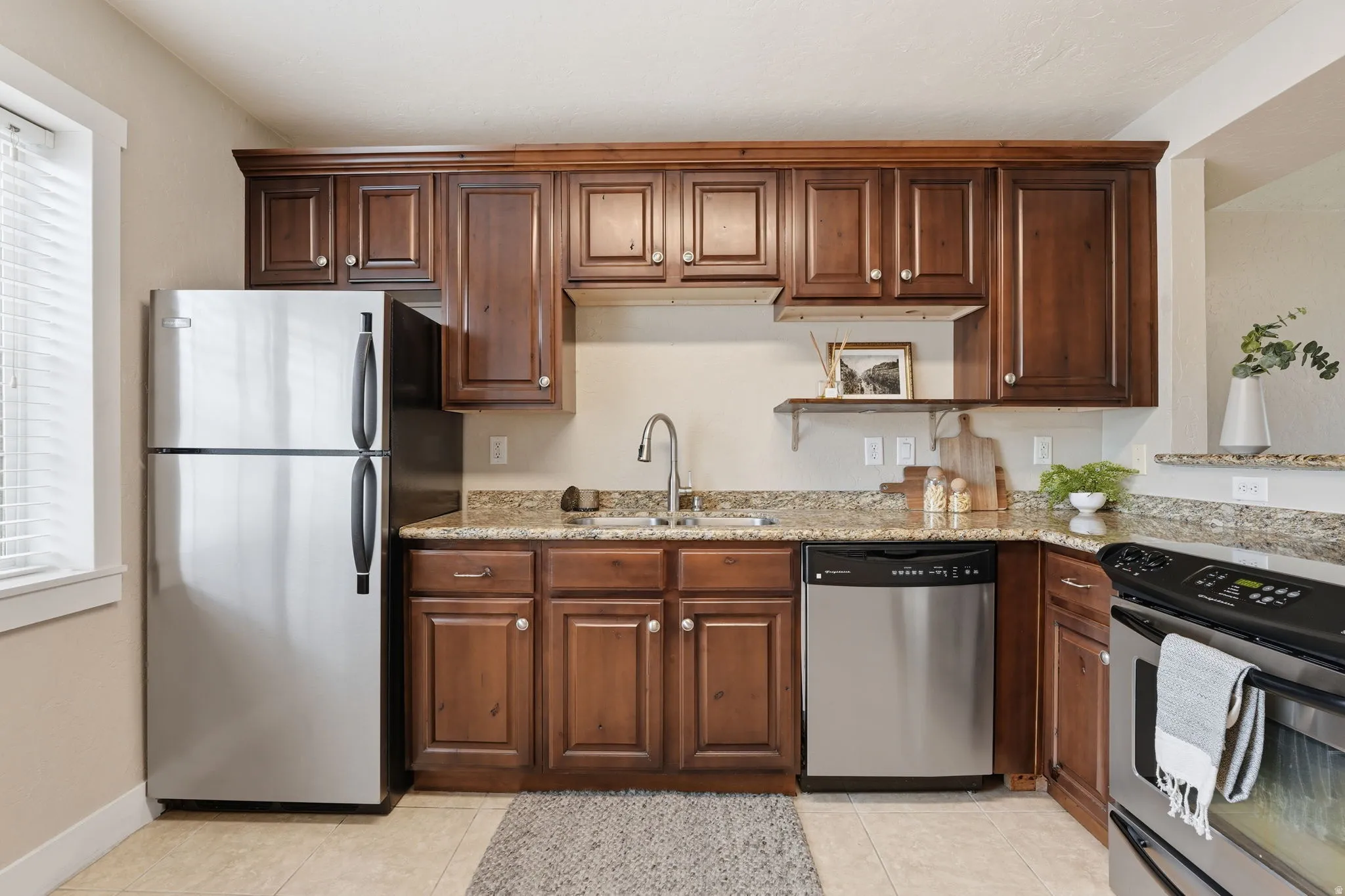 Kitchen with stainless steel appliances, light stone counters, and light tile patterned floors