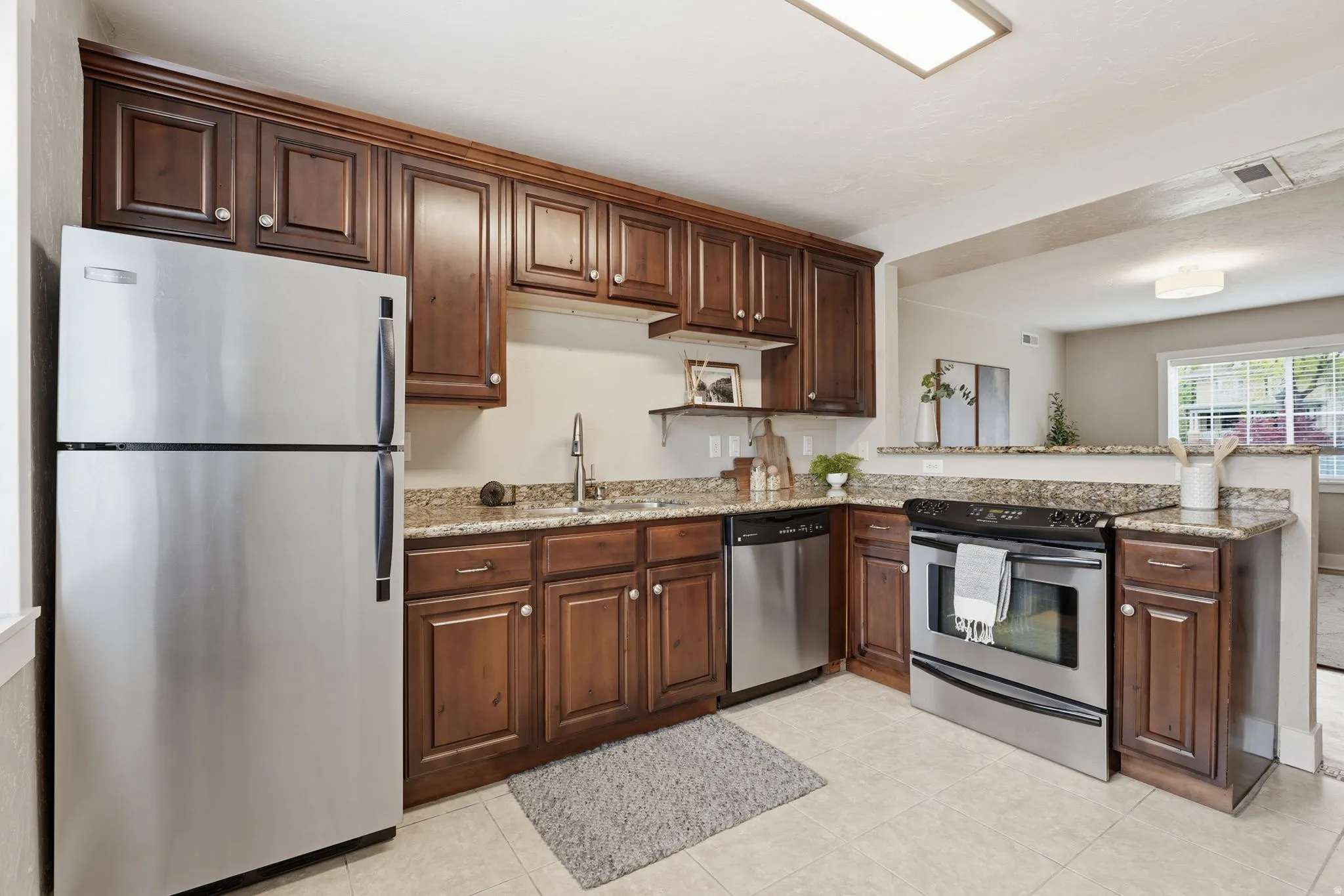 Kitchen with stainless steel appliances, light stone counters, dark wood finish cabinetry, and a peninsula
