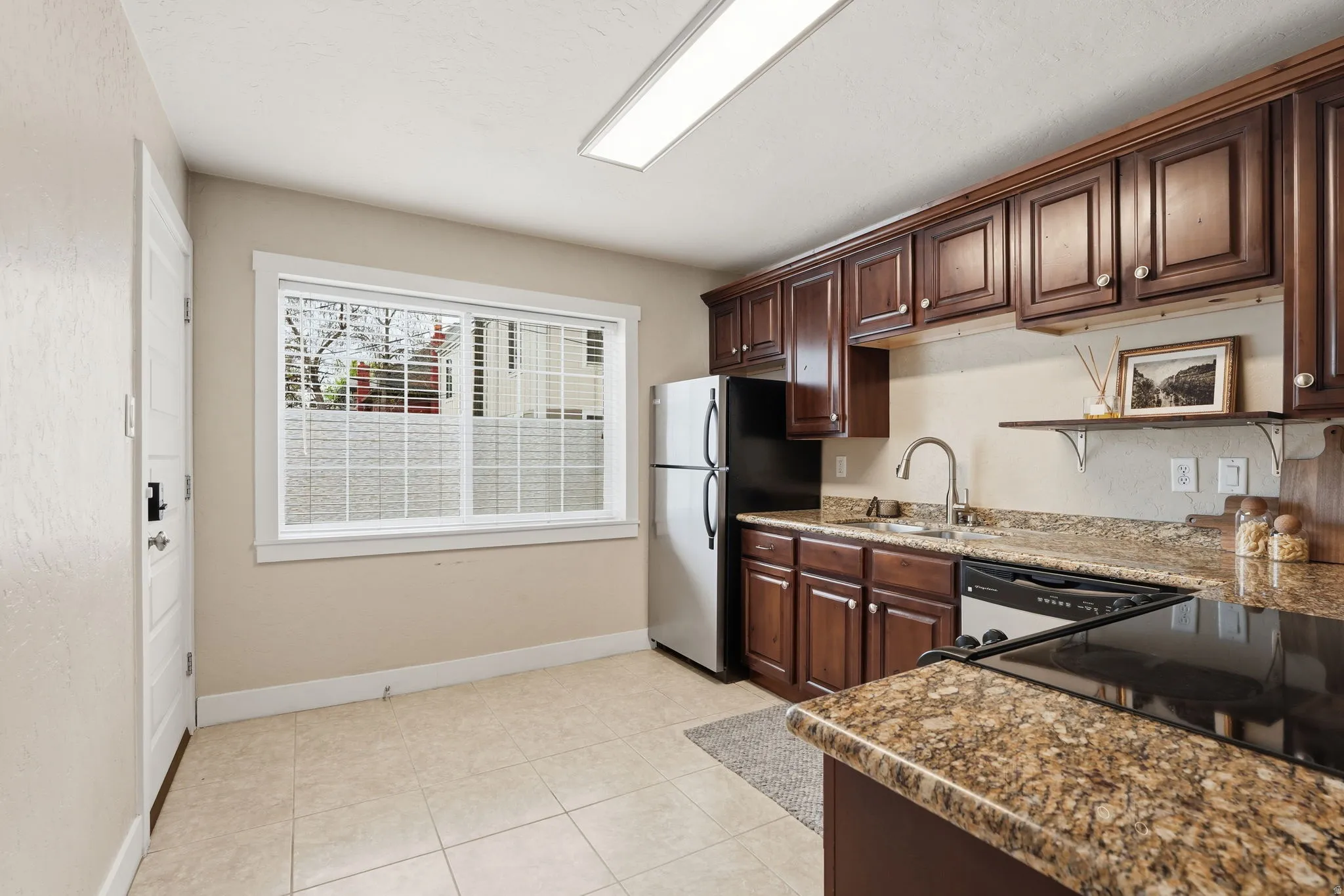 Kitchen with dark wood finish cabinetry, freestanding refrigerator, dark stone countertops, and light tile patterned floors