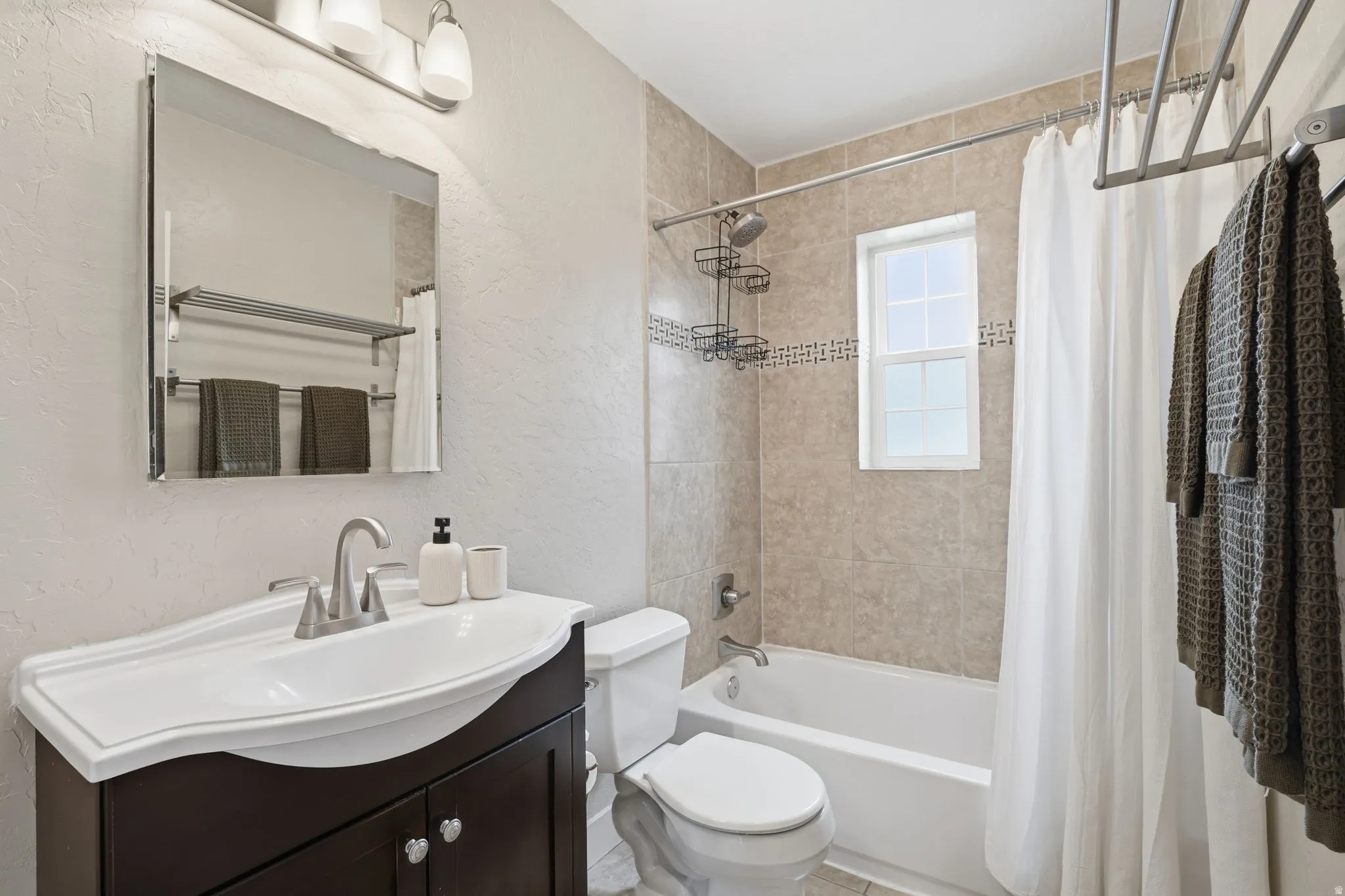 Bathroom with a textured wall, vanity, and shower / bathtub combination with curtain