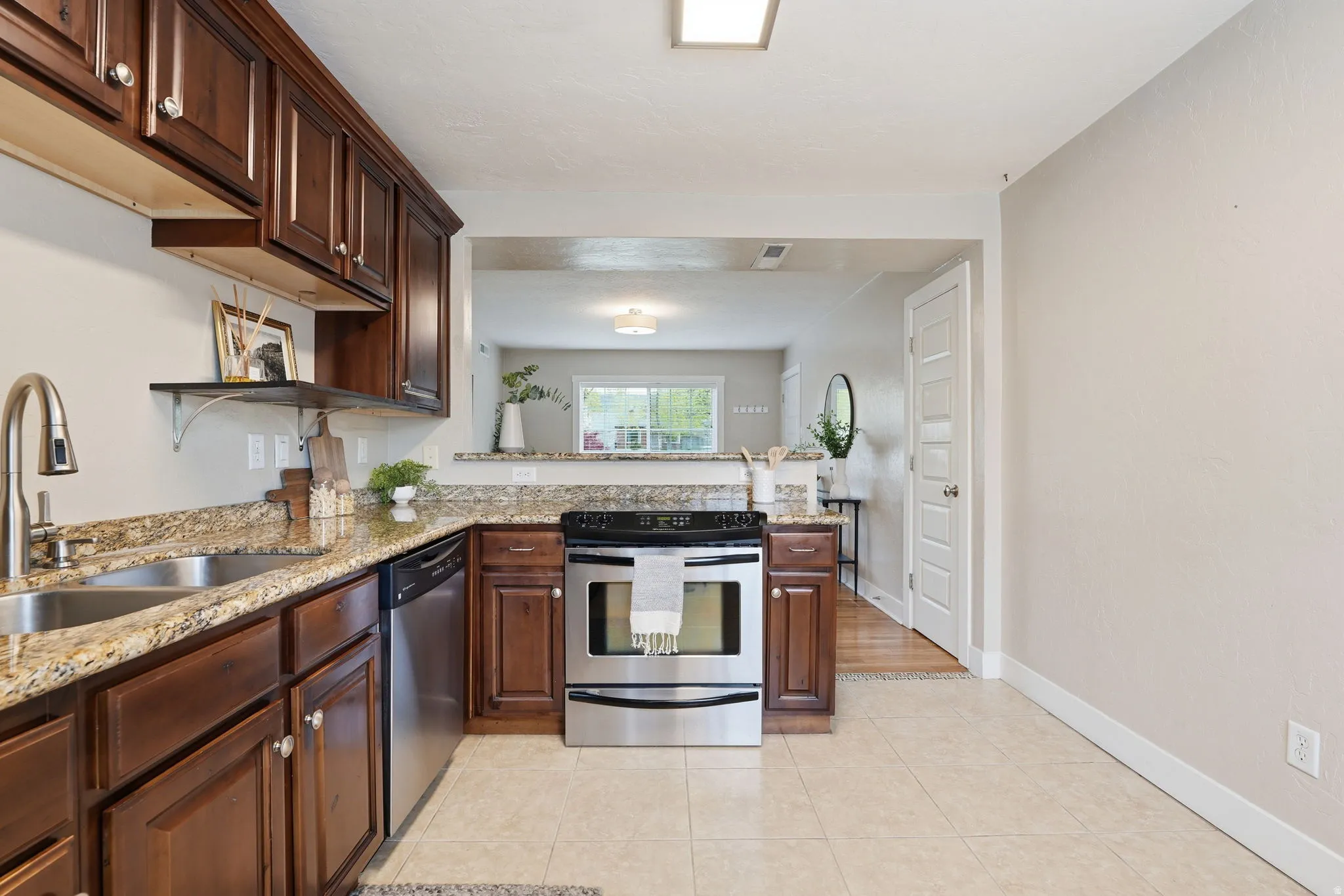 Kitchen with stainless steel appliances, light stone countertops, light tile patterned floors, dark wood finish cabinetry, and a peninsula