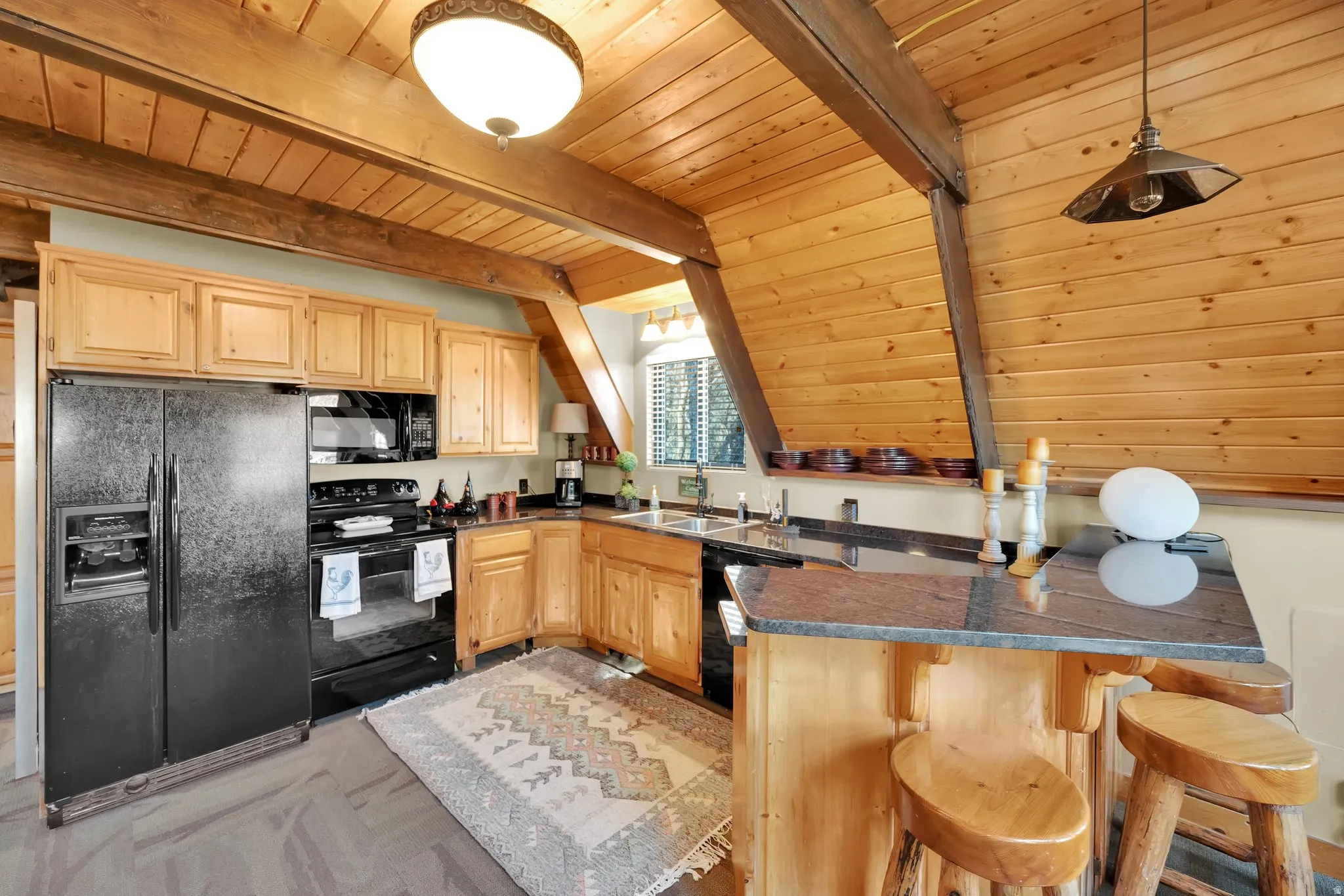 Kitchen with a peninsula, black appliances, light wood finish cabinets, a kitchen bar, and hanging light fixtures