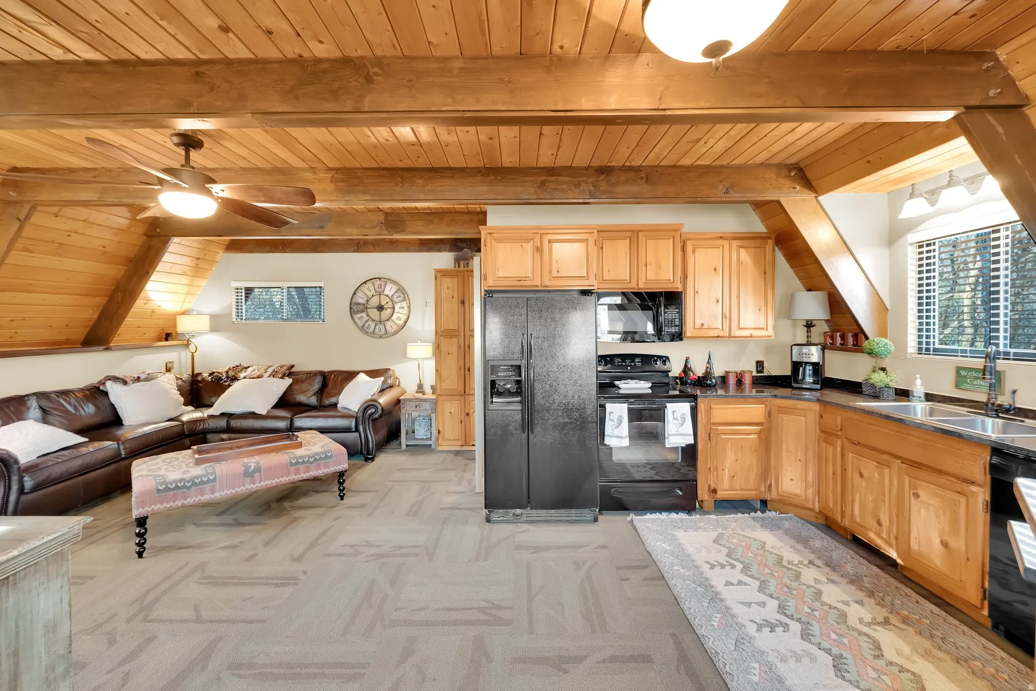 Kitchen with ceiling fan, open floor plan, black appliances, light colored carpet, and a wood ceiling with exposed beams