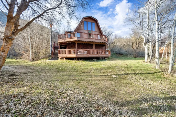 Back of house featuring a wooden deck, a lawn, and a gambrel roof