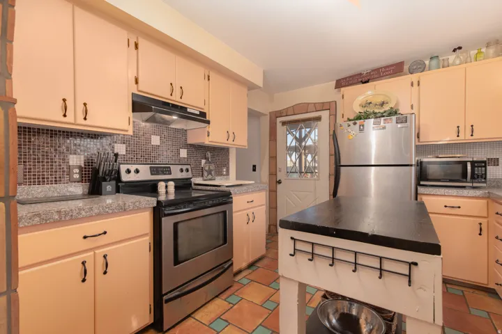 Kitchen with stainless steel appliances, backsplash, tile counters, and cream cabinets