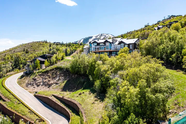 Hillside residence featuring stone and wood siding, multiple exterior balconies, and a snow-capped mountain backdrop