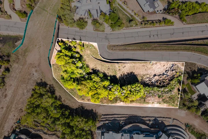 Expansive undeveloped lot featuring mature trees and varying topography, bordered by paved roadways and existing structures