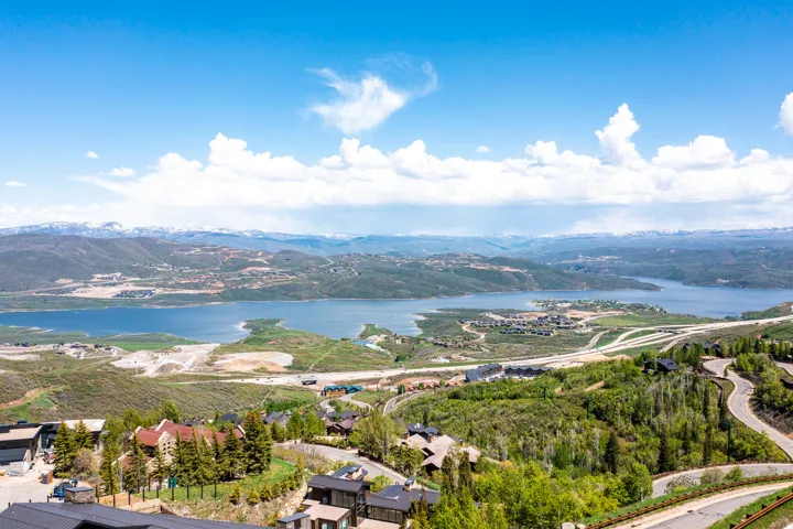 Expansive mountainous landscape featuring a large body of water, distant snow-capped peaks, and scattered residential properties