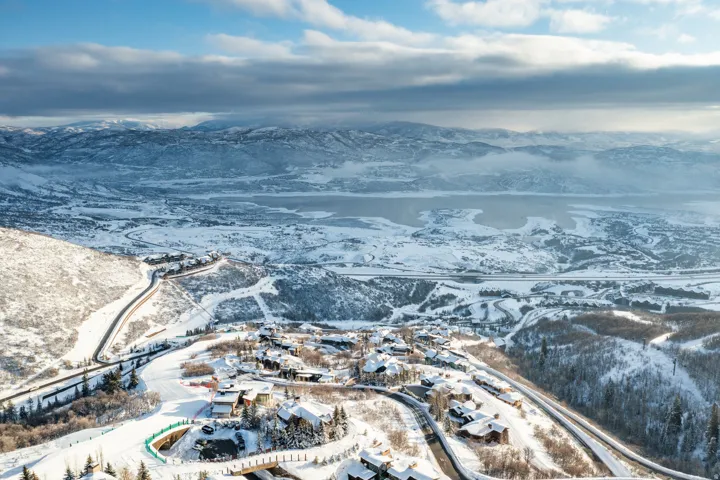 Snow-covered mountain landscape with residential properties, a body of water, and winding roads