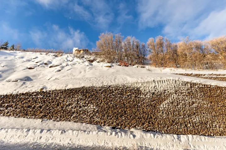 Layered gabion retaining walls provide structural support to the snow-covered hillside