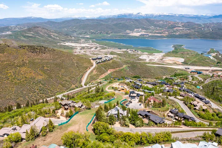 Expansive mountainous landscape featuring a large body of water, distant snow-capped peaks, and a developed hillside with multiple properties