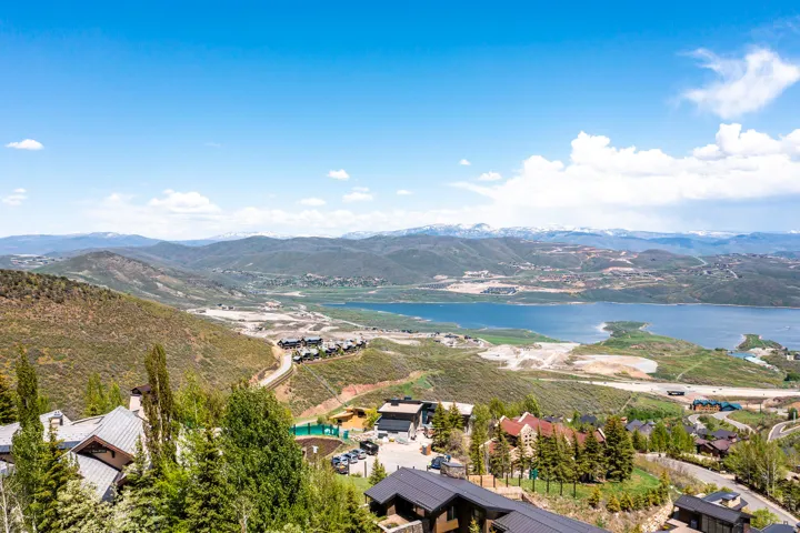 Expansive mountain landscape featuring a large body of water, distant snow-capped peaks, and scattered residential properties