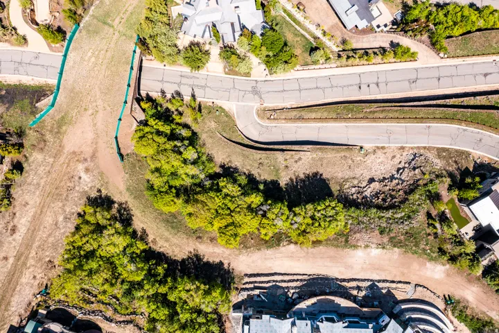 Aerial depiction of a sloped property featuring established roadways, surrounding residences, and natural landscaping