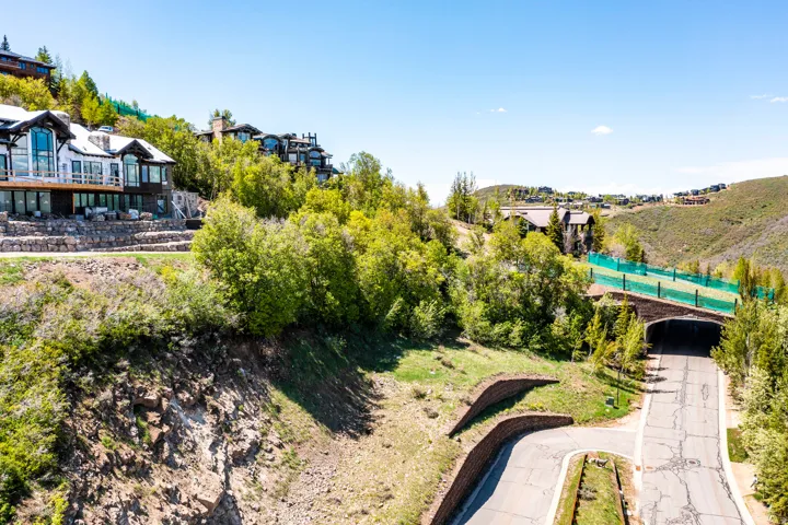 Hillside property featuring a multi-level residence with extensive glass windows, a large balcony, and stone retaining walls