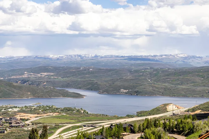 Expansive landscape featuring a large body of water, distant snow-capped mountains, and rolling green hills