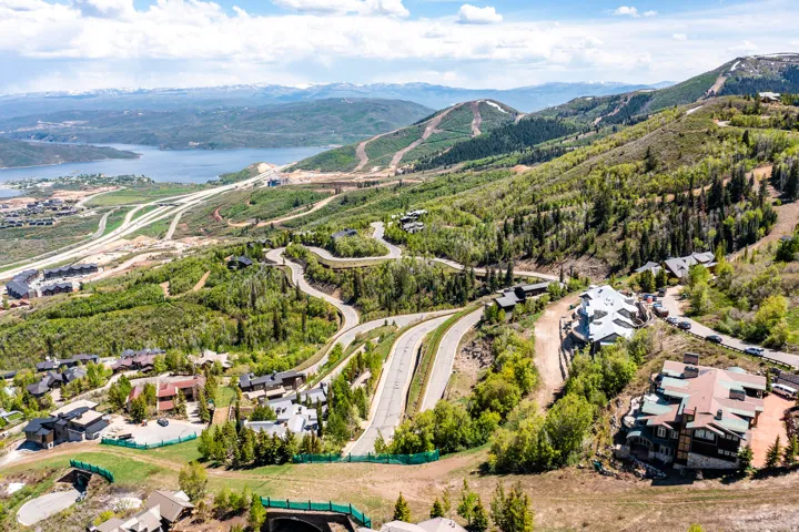 Sweeping mountain landscape featuring established residential properties, winding roadways, abundant mature trees, a distant lake, and snow-capped peaks