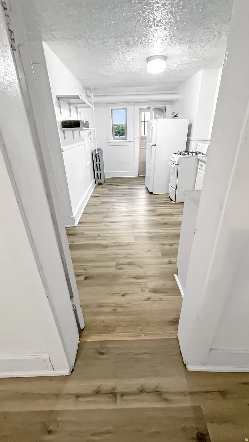 Hallway featuring light wood-type flooring, a textured ceiling, and radiator