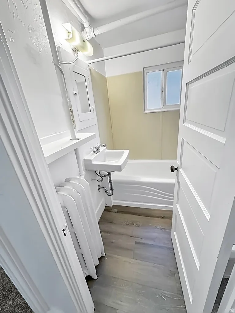 Full bath with wood finished floors, radiator heating unit, and  shower combination