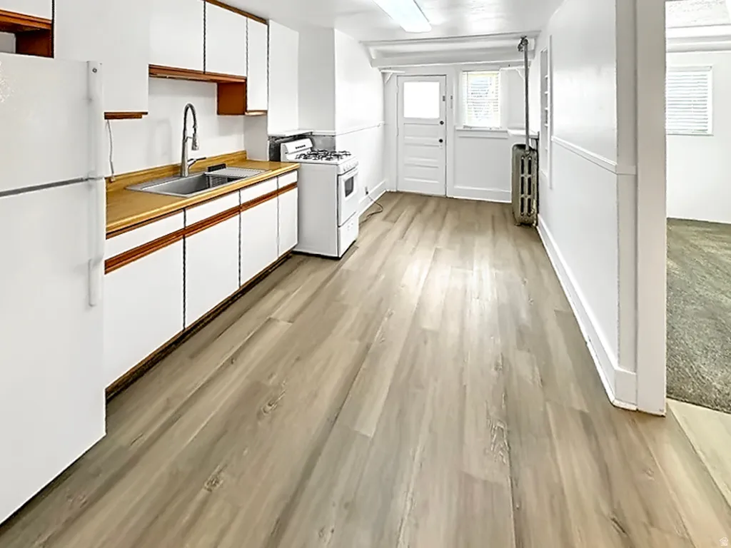 Kitchen featuring dual tone cabinets, white appliances, light wood finished floors, light countertops, and radiator