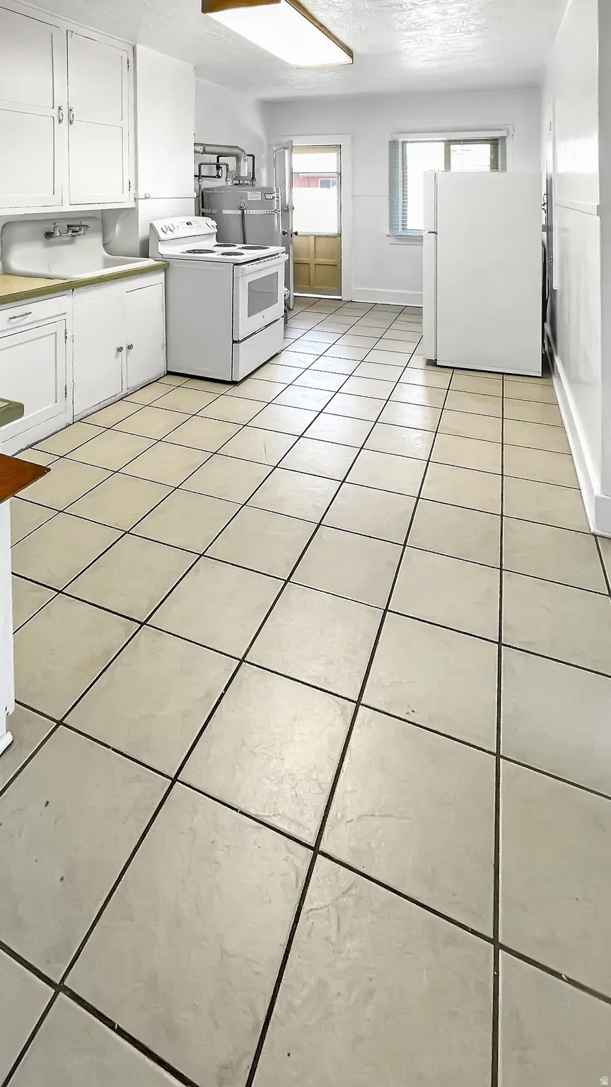 Laundry area with light tile patterned floors, a textured ceiling, and water heater